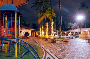 A playground with a slide and climbing structures, a pool area with lounge chairs, and palm trees. - Tequendama Hotel Campestre Villavicencio (Villavicencio)