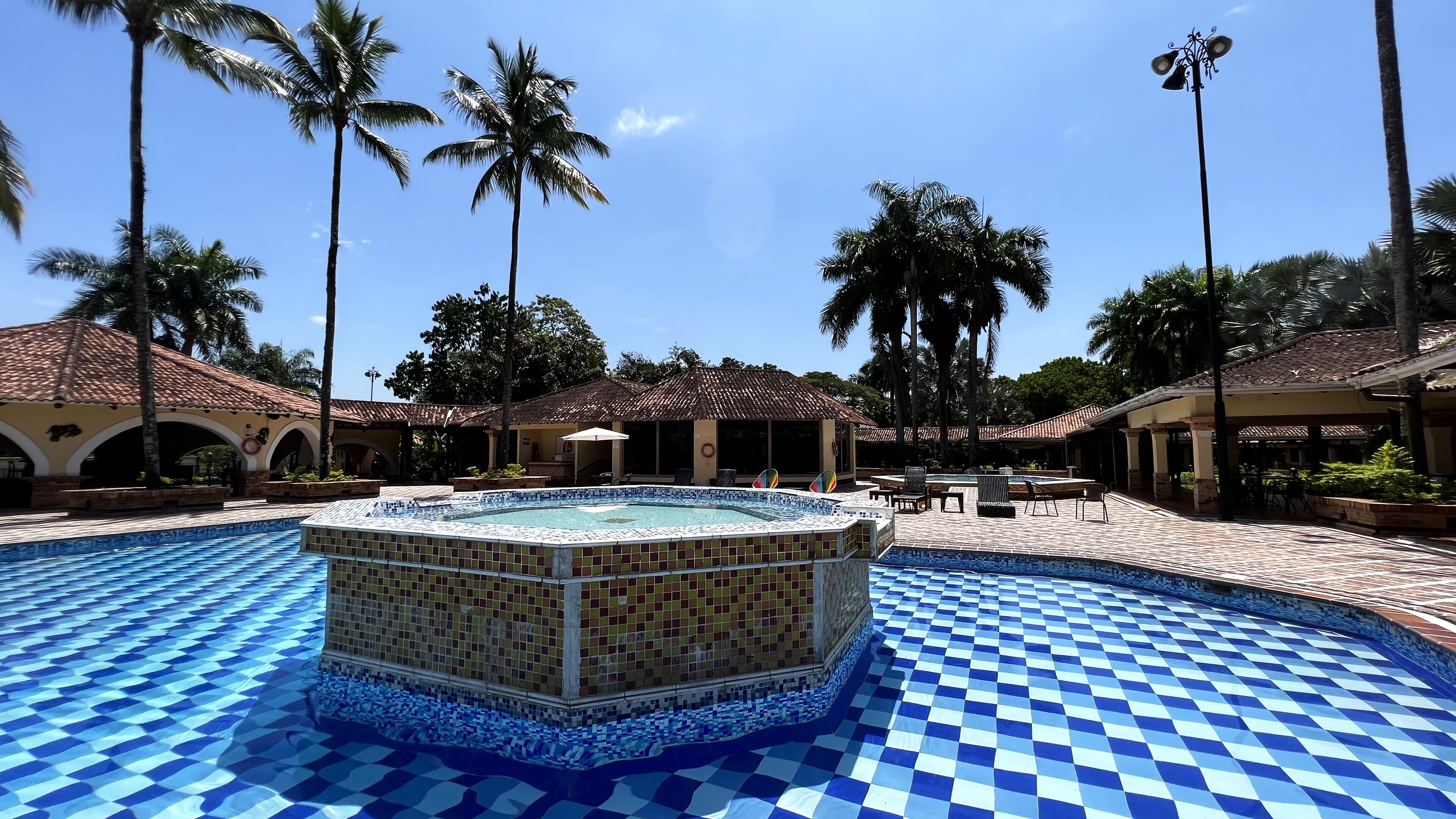 A pool area with a tiled hot tub surrounded by palm trees and covered seating areas.