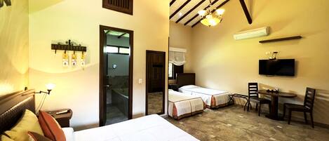 A hotel room with a large bed, a desk with a chair, a television, and a bathroom visible through an open door.