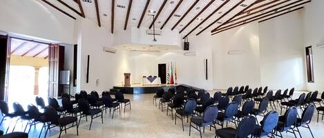 Un salón de conferencias con filas de sillas orientadas hacia un escenario con un atril y banderas.