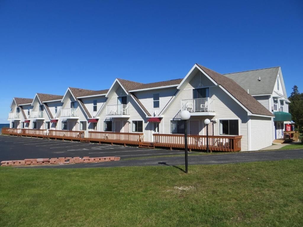 A row of white motel buildings with balconies and a parking lot in front.