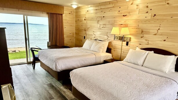 A room with two beds, a wooden wall, a window with curtains, and a view of the sea. - Bridge View Motel & Condo's (Mackinaw City)