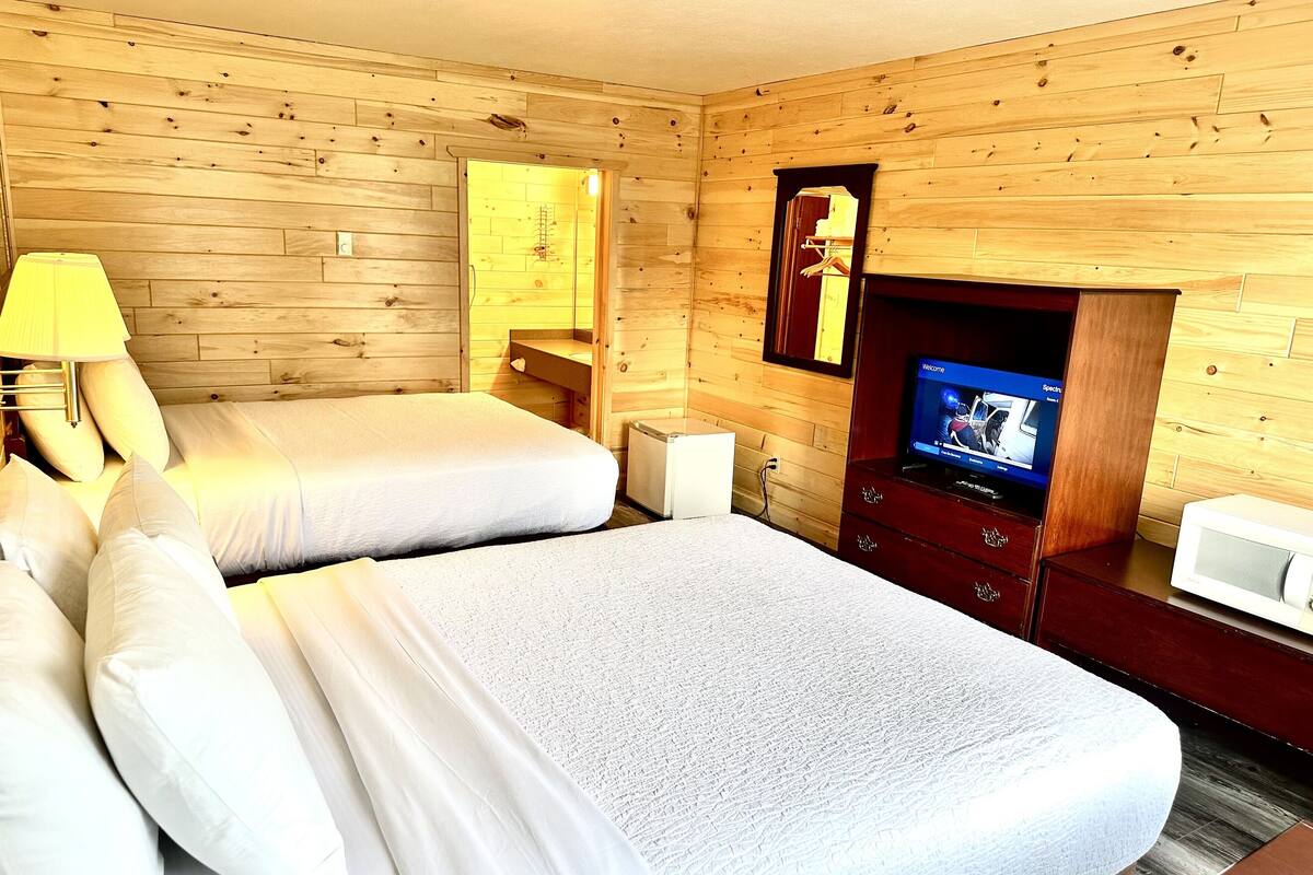 A wooden cabin room with two beds, a television, a small table, and a wooden wall.