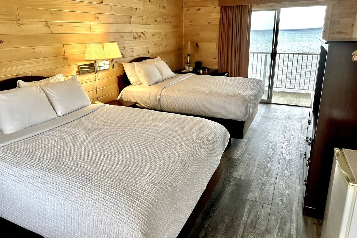 A hotel room with two beds, wooden walls, a balcony with a view of the sea, and a refrigerator.