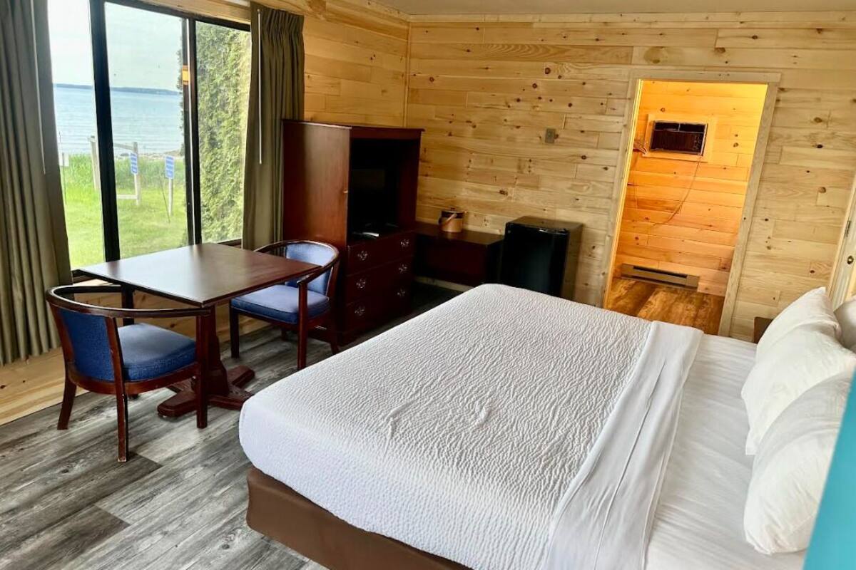 A wooden cabin room with a bed, a desk, and a chair.