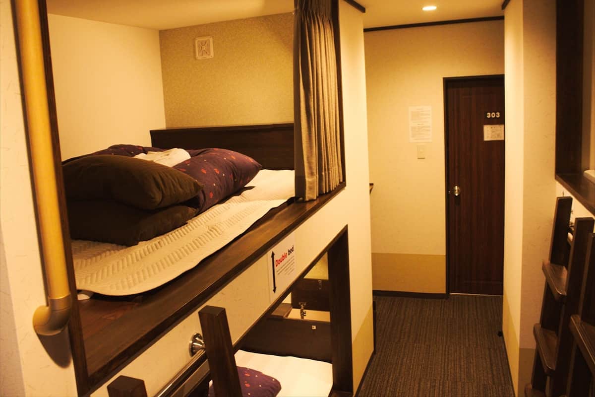 A hotel room with a bunk bed, a single bed, a door with a number, and a small window.