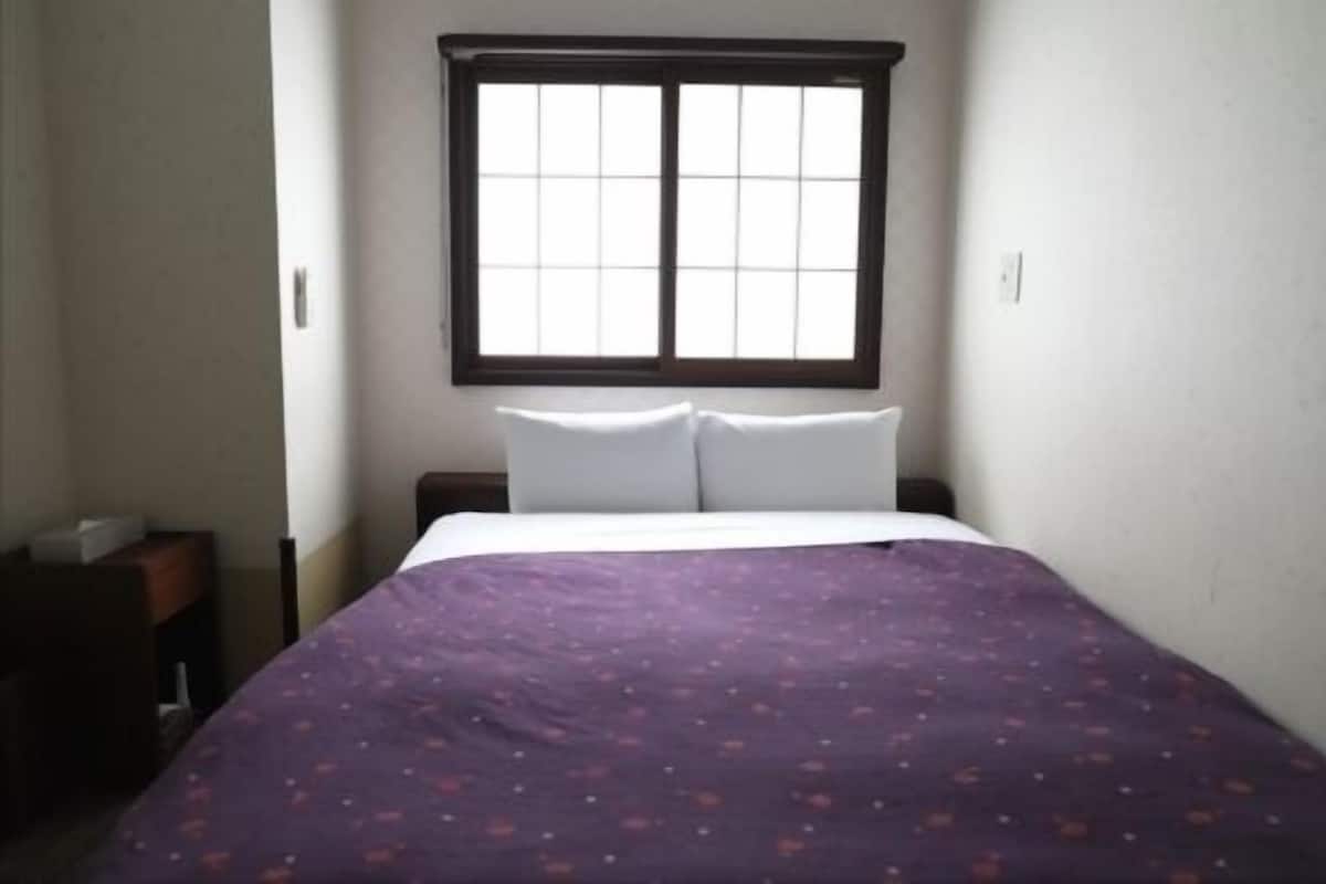 Un dormitorio con una cama, una ventana y una mesita de noche.
