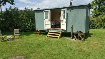 A small, green metal structure with an open door revealing a bed and a chair inside.