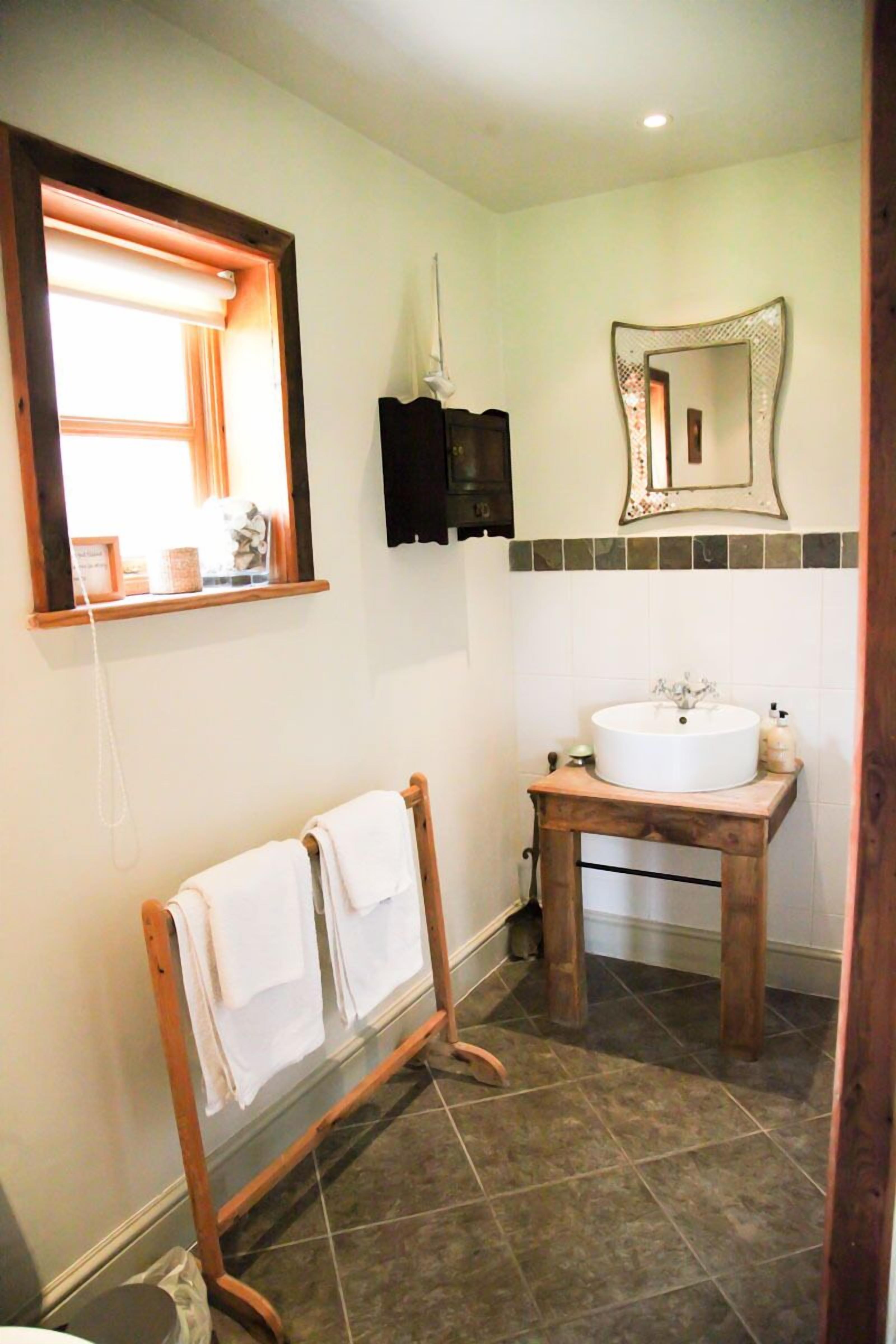 A bathroom with a wooden vanity, a white sink, a mirror, and a towel rack.