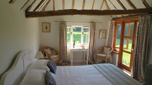 Une chambre à coucher avec un grand lit, deux chaises, une petite table et une fenêtre avec des rideaux.