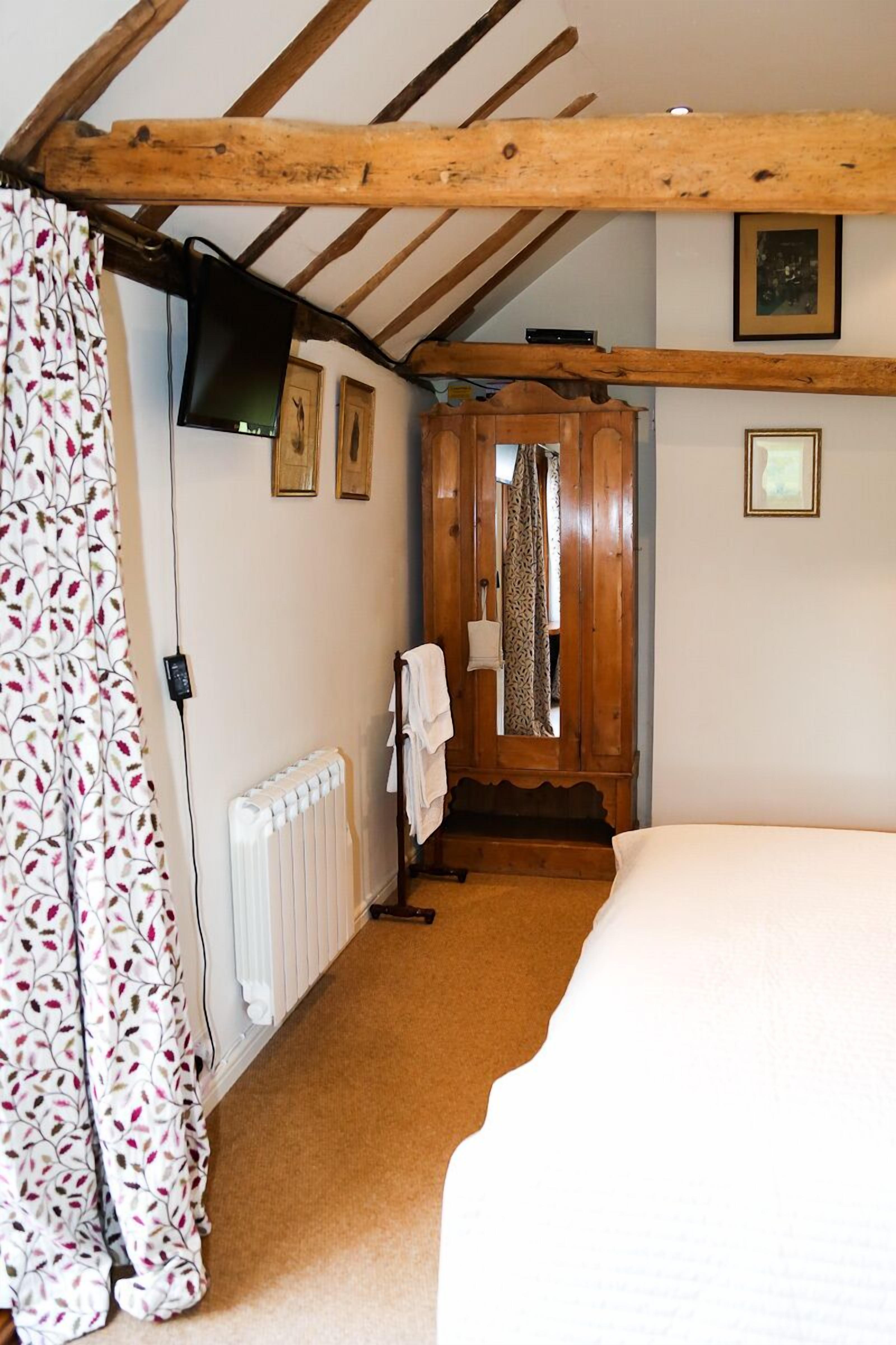 A bedroom with a wooden ceiling, a bed, a radiator, a television, and a door with a mirror.