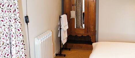 A bedroom with a wooden ceiling, a bed, a radiator, a television, and a door with a mirror.