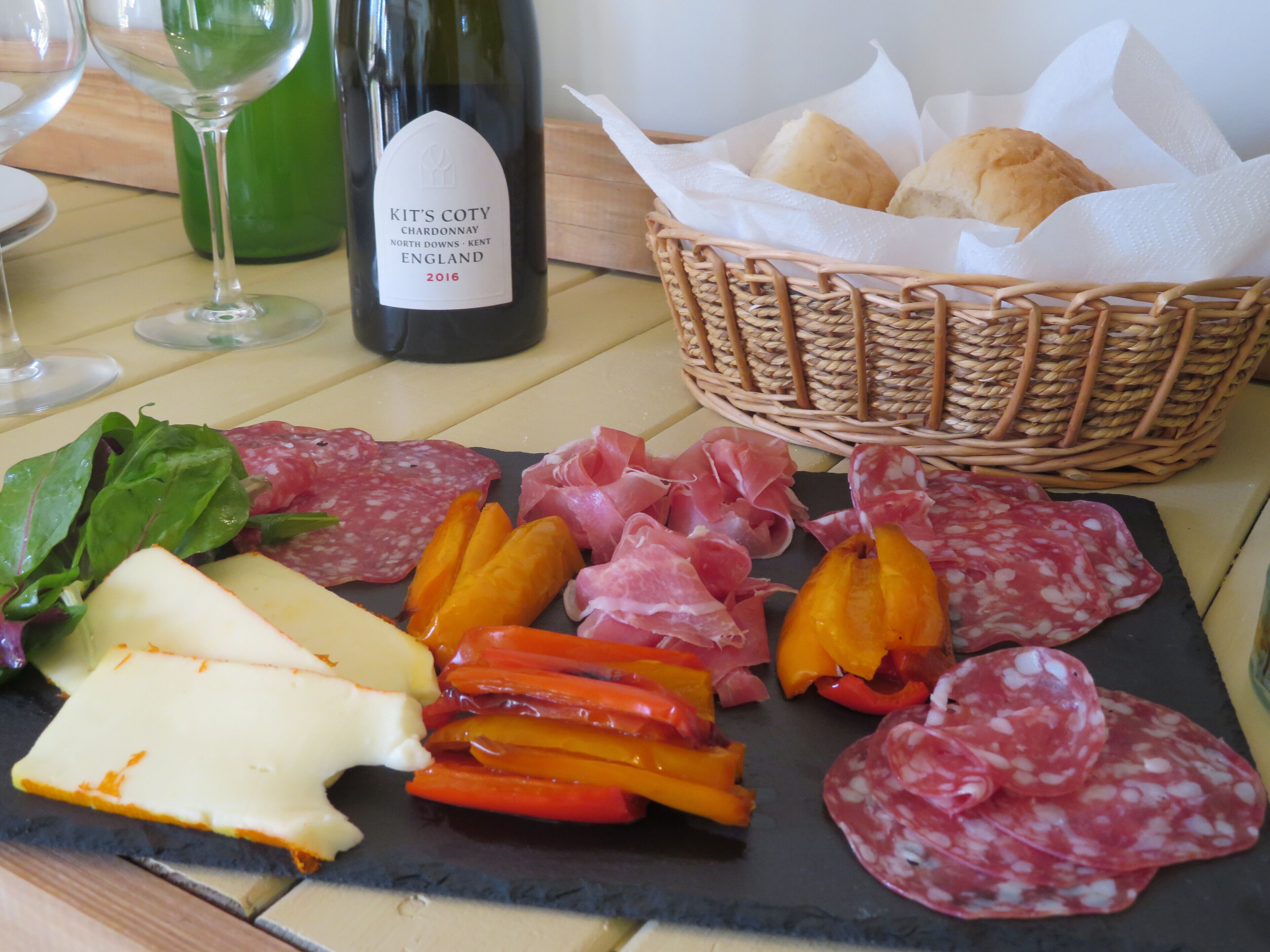 A charcuterie board with various meats, cheeses, and vegetables, accompanied by a bottle of wine and a basket of bread.