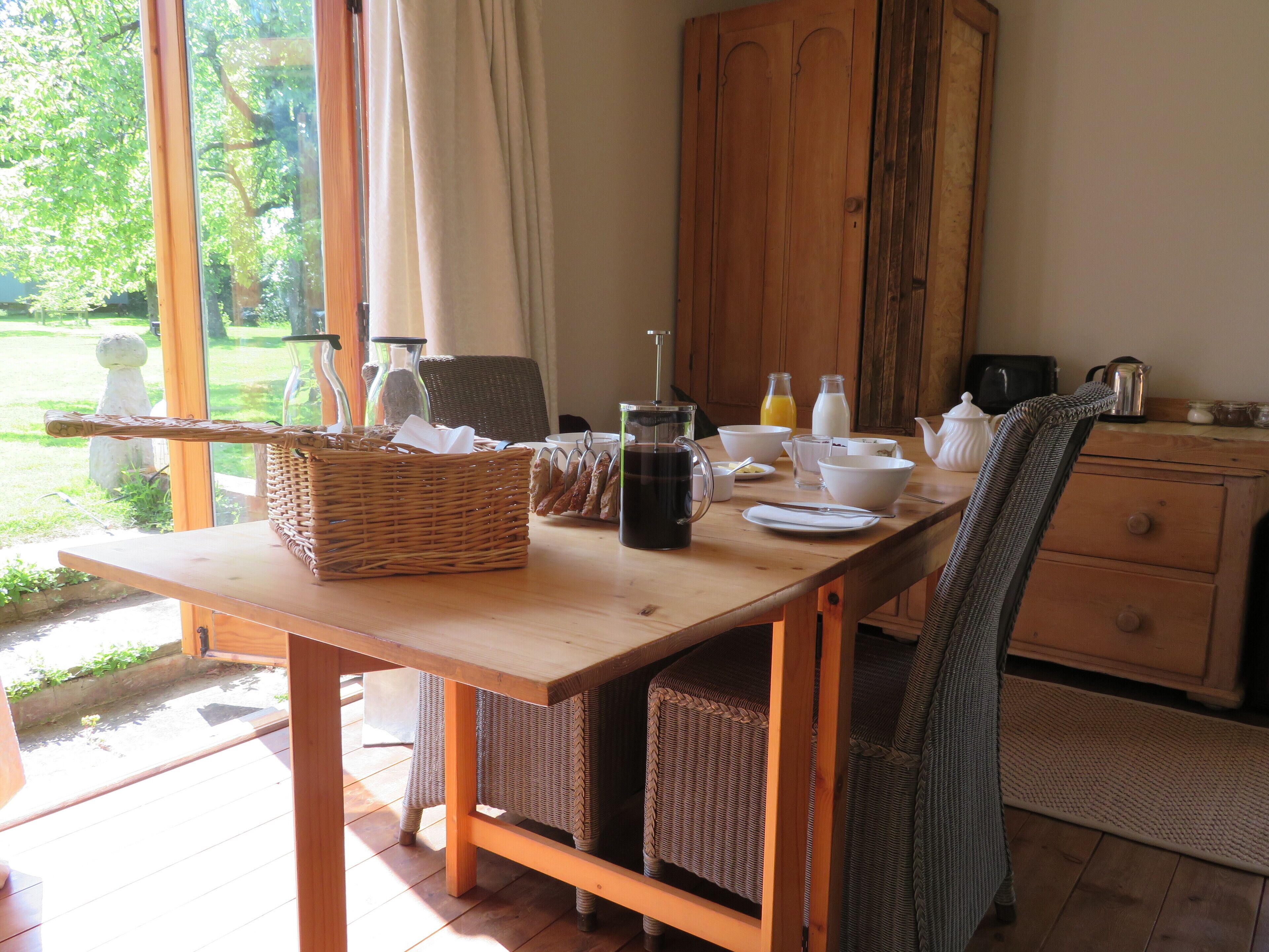 A breakfast table with wicker baskets, bowls, cups, and a coffee pot.