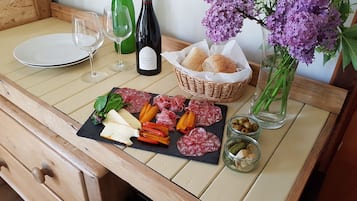 Ett träbord med en svart skifferplatta där olika sorters ostar, lufttorkat kött och oliver är uppradade. En vinflaska, ett vinglas och en korg med brödbullar syns också.
