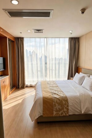 Ein Hotelzimmer mit einem großen Bett, einem Fernseher, einem Kleiderschrank und Blick auf die Stadt.