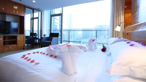 A hotel room with a large bed, a TV, a desk, and a view of the city.