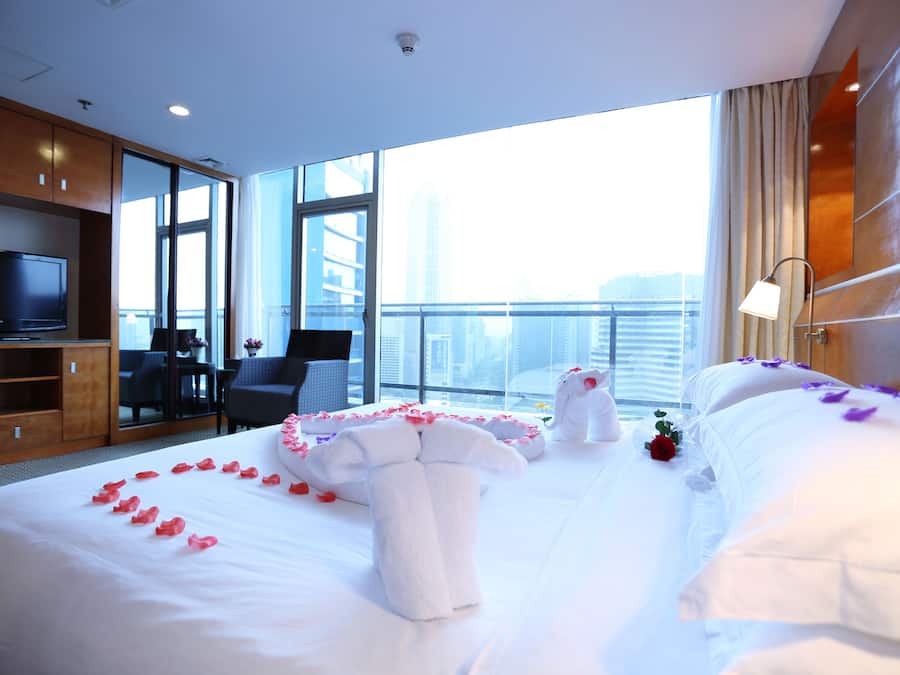 Quarto de hotel com uma cama grande, televisão, escrivaninha e vista para a cidade.