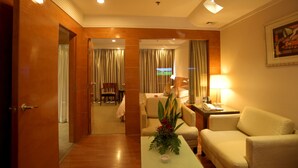 A hotel room with a wooden floor, a sofa, a table with a vase of flowers, a lamp, and a painting on the wall.