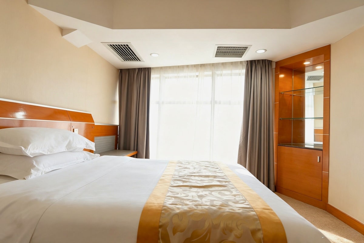 A hotel room with a bed, a nightstand, a mirror, and a window with curtains.