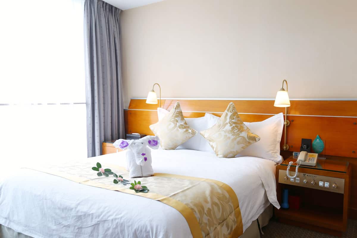 Ein Hotelzimmer mit einem ordentlich bezogenen Bett, einem Nachttisch mit Lampe und einem weiteren Nachttisch mit Telefon.
