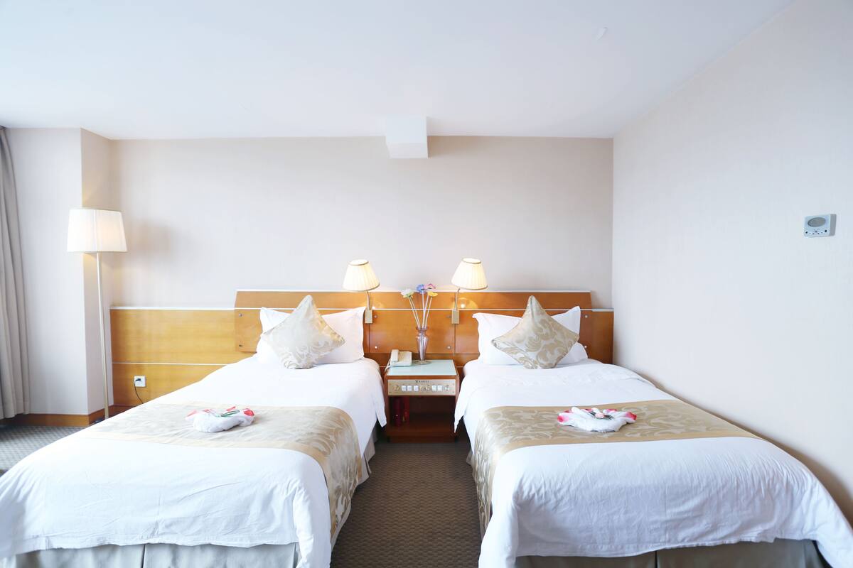Una habitación de hotel con dos camas individuales, una mesita de noche con lámpara y una pequeña mesa con un jarrón de flores.