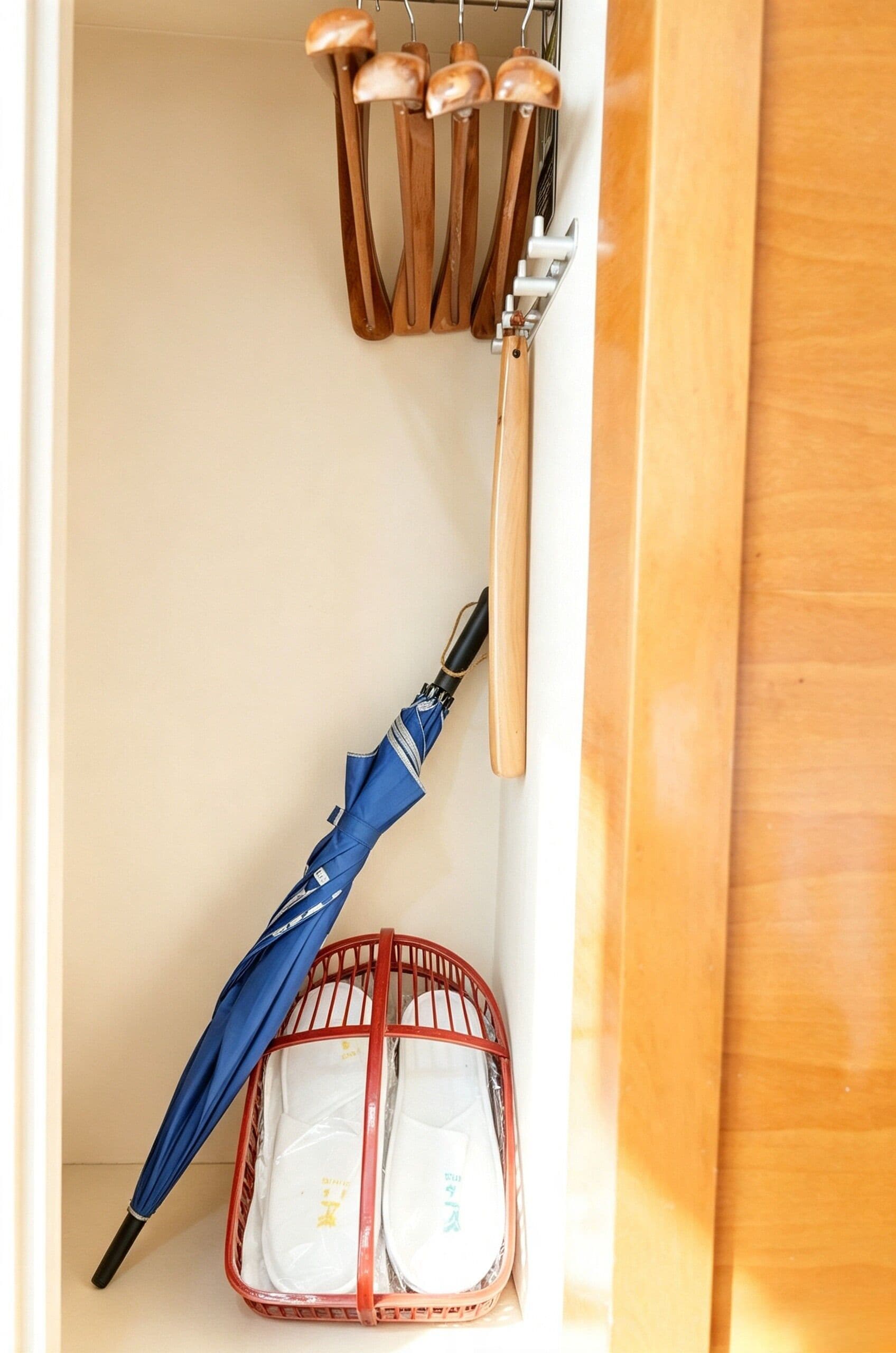A storage area with a blue umbrella, a red basket, and wooden utensils hanging on a rack.
