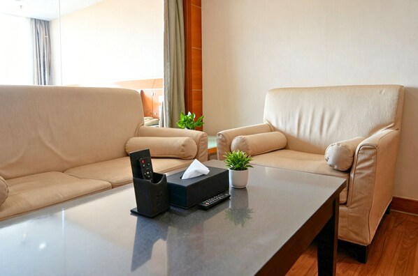 A hotel room with two beige sofas, a coffee table, a remote control, a tissue box, and a small potted plant. - Yihe Hotel Ouzhuang (Guangzhou)
