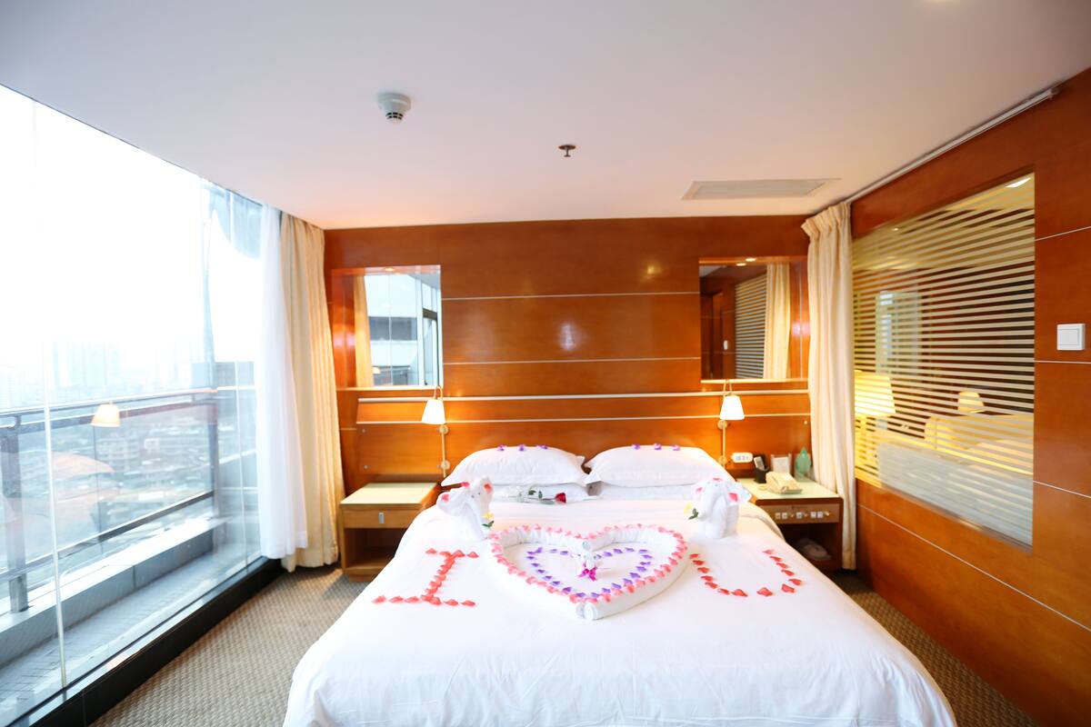 Ein Hotelzimmer mit einem großen Bett, einem Nachttisch, einem Spiegel und einem Fenster mit Vorhängen.