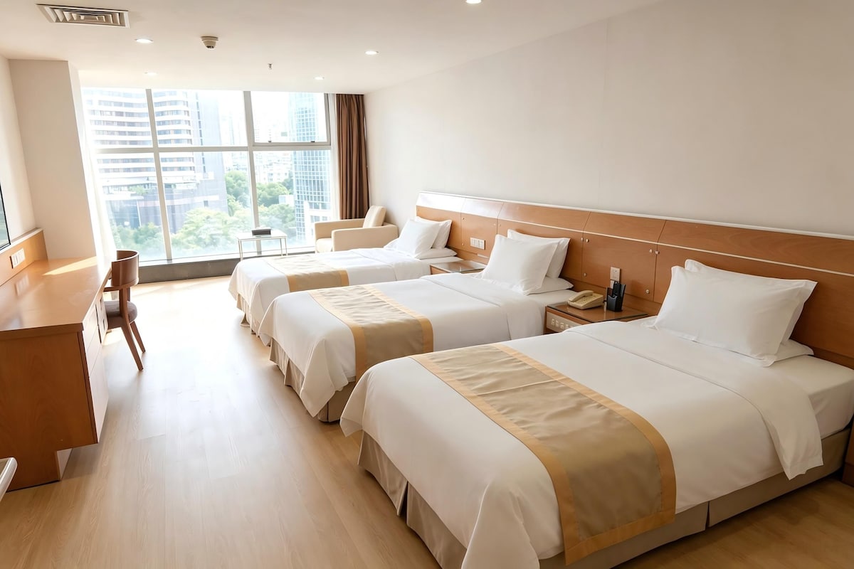 A hotel room with three beds, a desk, and a view of the city.