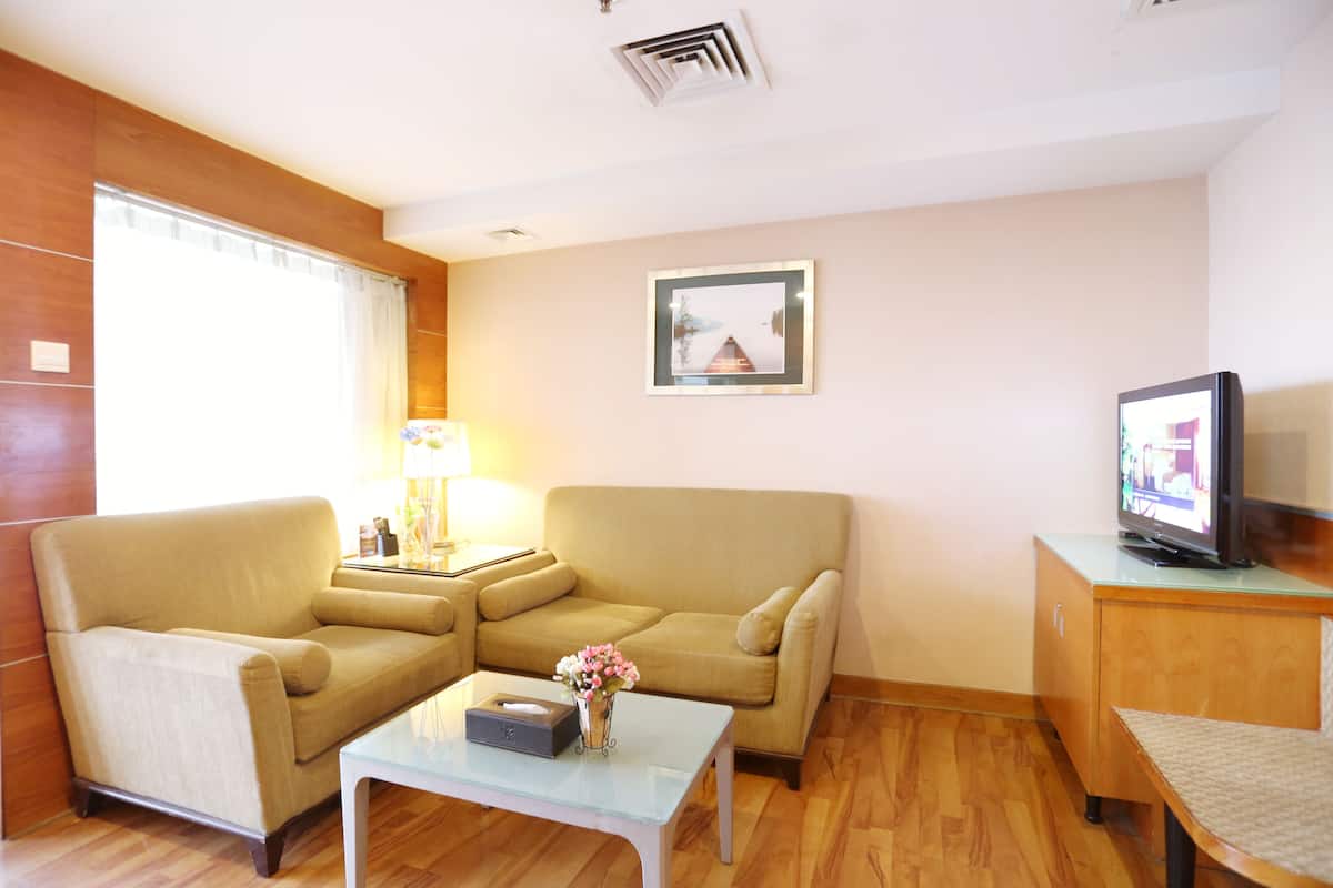 Ein Wohnzimmer mit einem beigefarbenen Sofa, einem Glastisch, einem Fernseher auf einer Holzkommode und einem gerahmten Bild an der Wand.