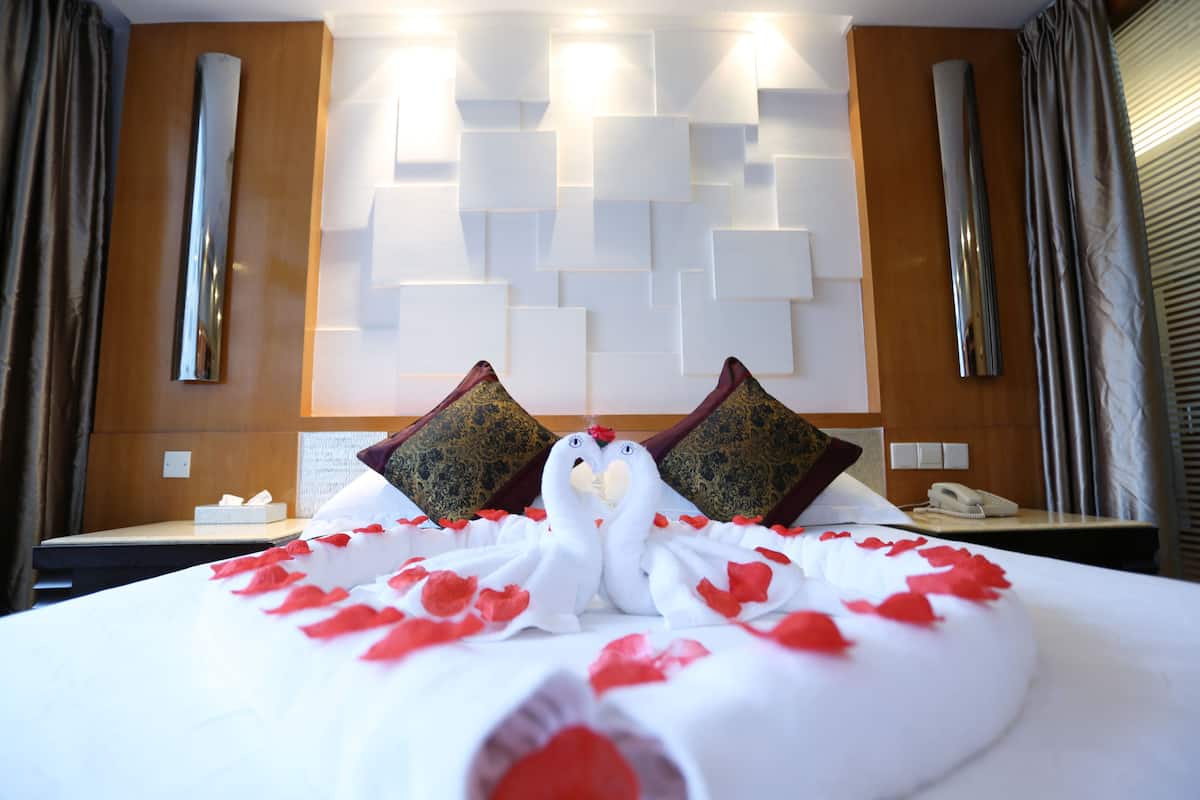 Ein Hotelzimmer mit einem Bett, das mit Rosenblättern und zwei schwanenförmigen Kissen dekoriert ist.