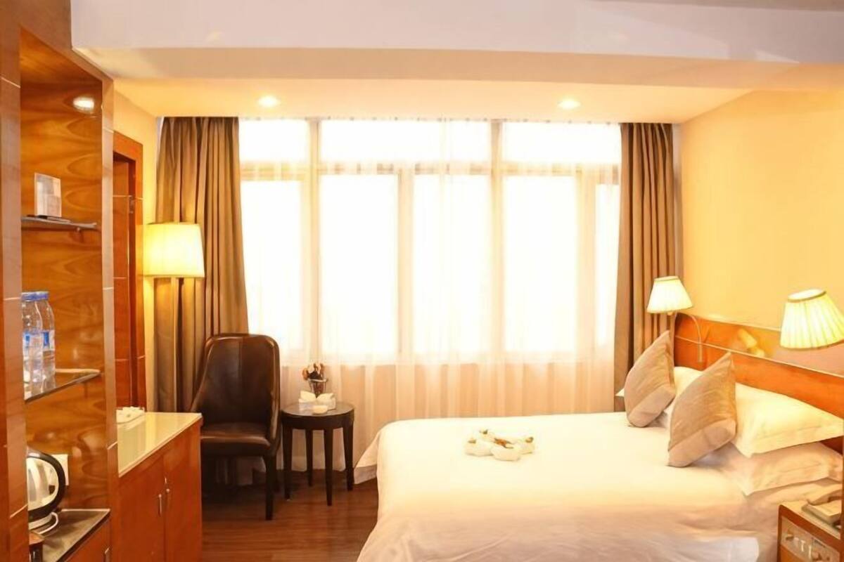 Ein Hotelzimmer mit Bett, Schreibtisch, Stuhl, einem kleinen Tisch mit Lampe und einem Fenster mit Vorhängen.