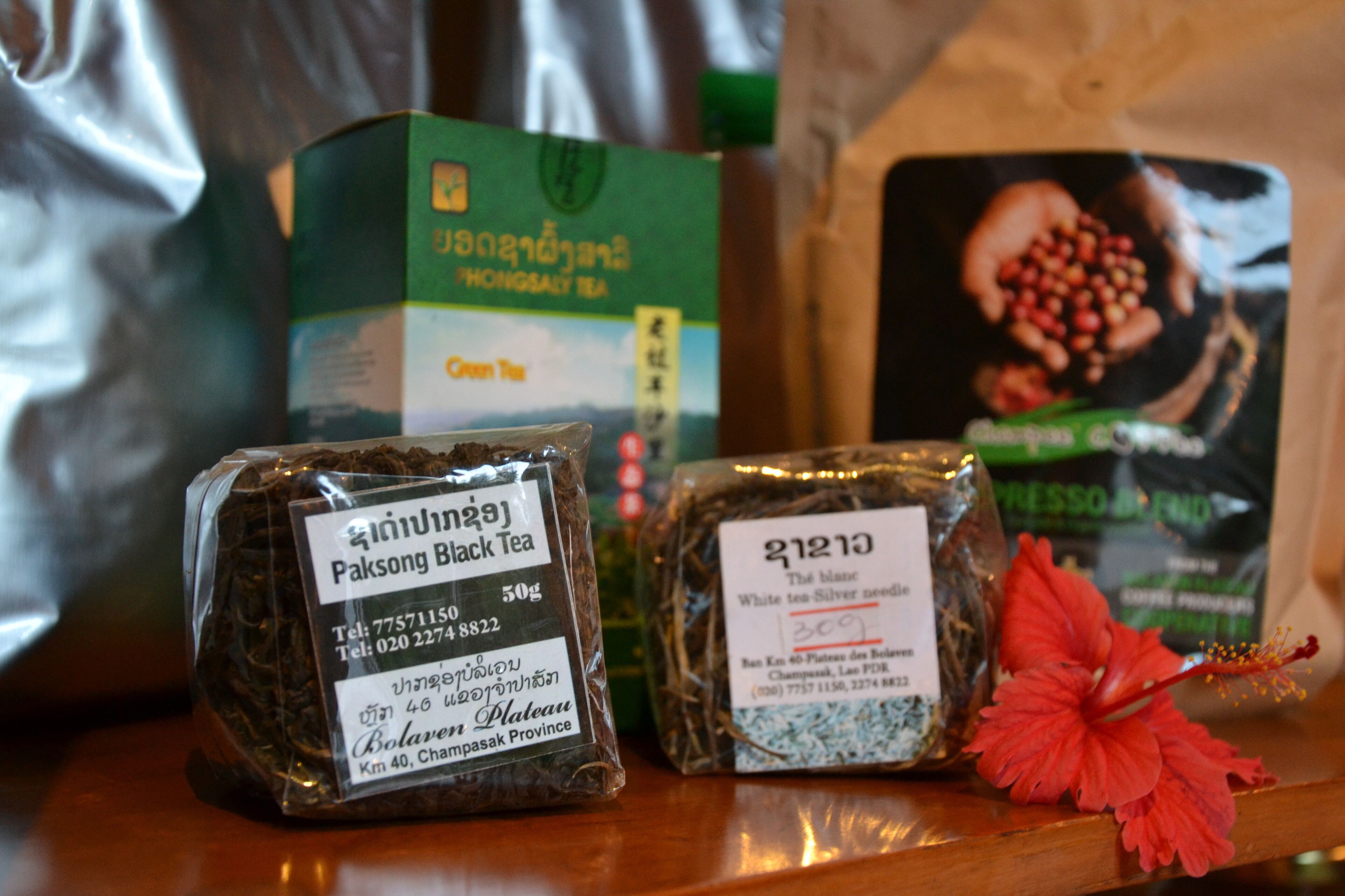 Three packaged teas on a wooden surface with a red hibiscus flower.
