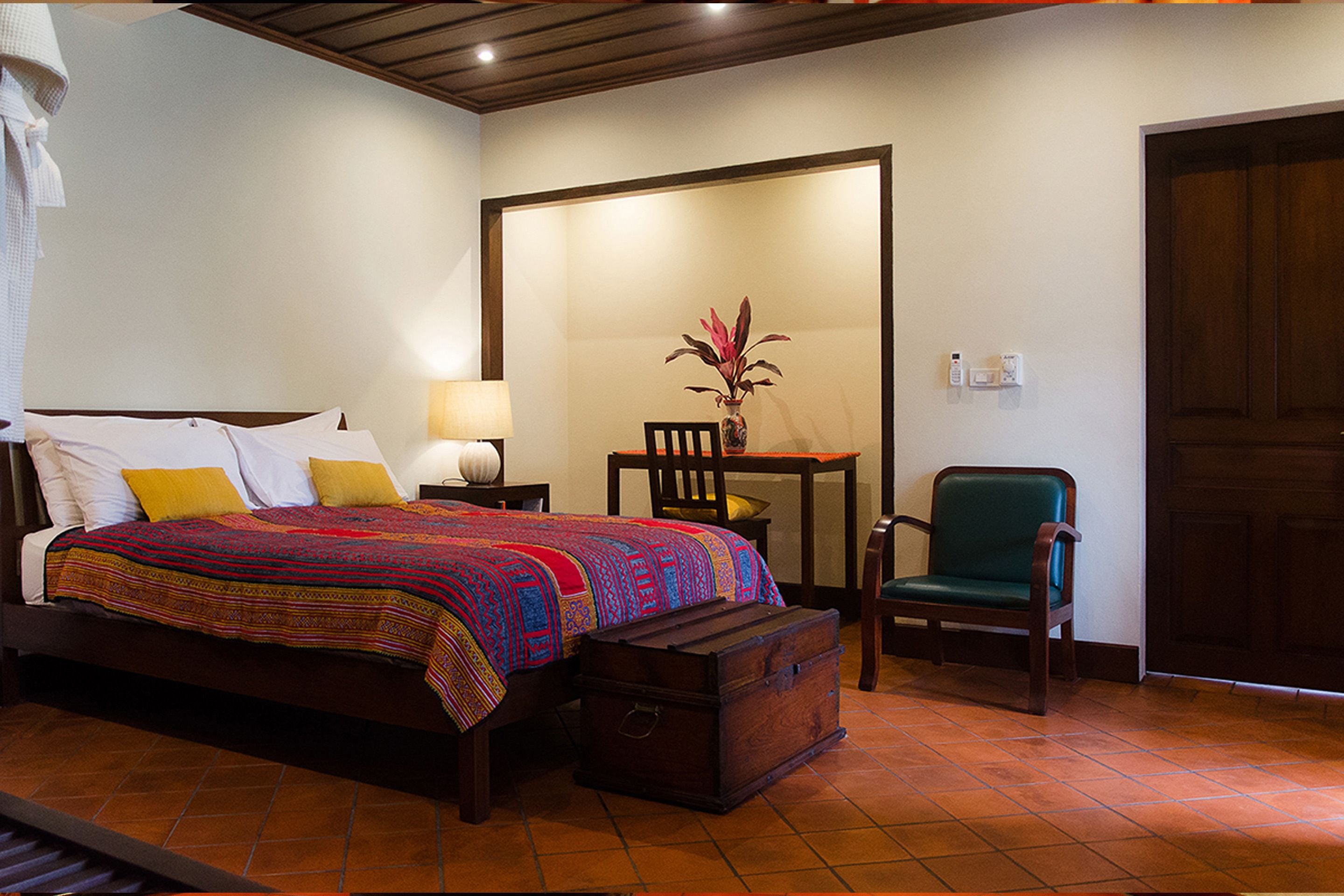 Habitación de hotel con cama, escritorio, silla, un jarrón con flores y una puerta de madera.