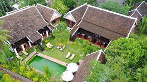 A traditional villa with a swimming pool, surrounded by lush greenery and palm trees.