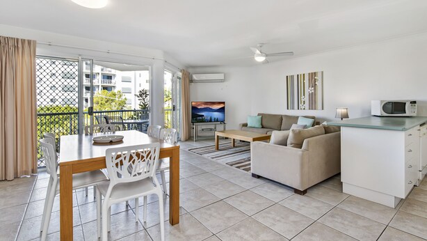 A modern living room with a dining area, a sofa set, a TV, and a kitchen area with a microwave. - Dockside Mooloolaba (Mooloolaba)