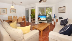 A living room with a sofa, coffee table, and a television. There is a dining area with chairs and a table. - Dockside Mooloolaba (Mooloolaba)