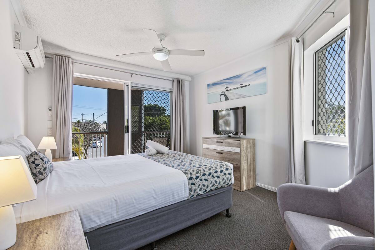 A modern hotel room with a bed, a desk, a television, and a balcony with a view.