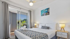 A bedroom with a bed, two bedside tables with lamps, a painting on the wall, and a sliding glass door leading to an outdoor area. - Dockside Mooloolaba (Mooloolaba)