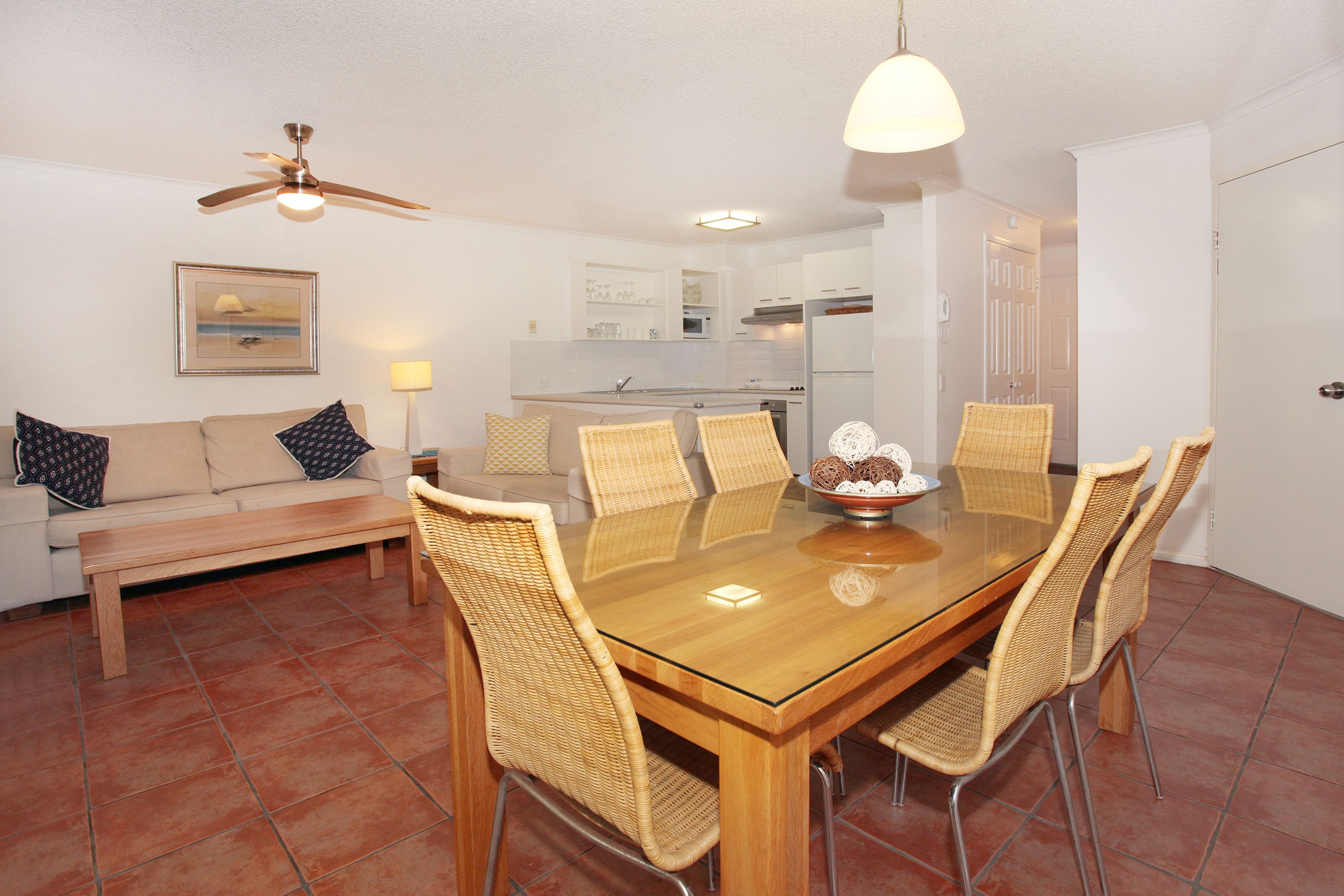 A dining area with a wooden table, wicker chairs, a bench, and a ceiling fan.