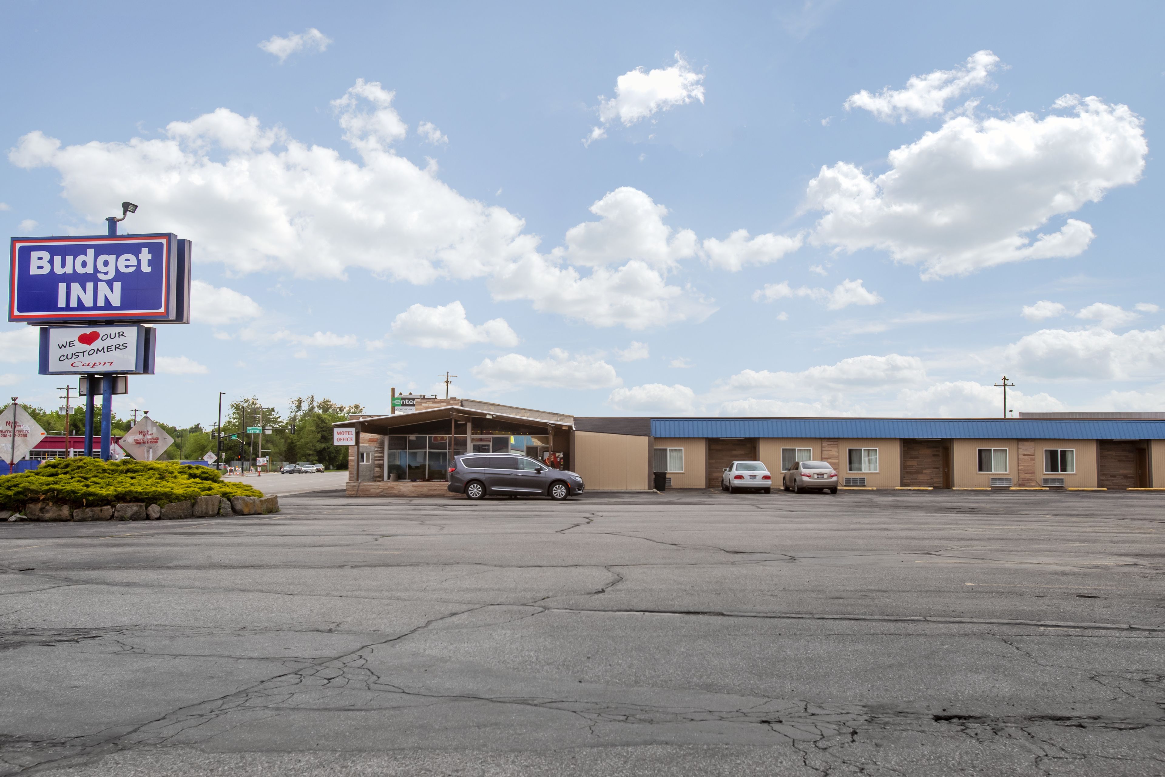 A Budget Inn with a parking lot, a building with a blue roof, and a clear sky with clouds.