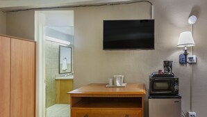 A compact kitchen with a wooden cabinet, a microwave, a coffee machine, and a TV mounted on the wall.