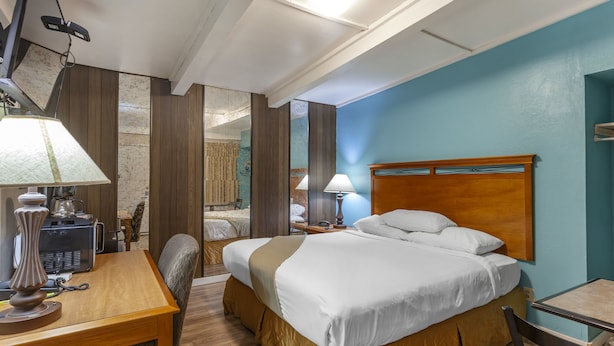 A hotel room with a bed, a desk, a chair, a lamp, and a mirror.