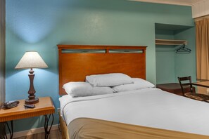 A neatly made bed with white linens, a wooden bedside table with a lamp, a phone, and a remote control.