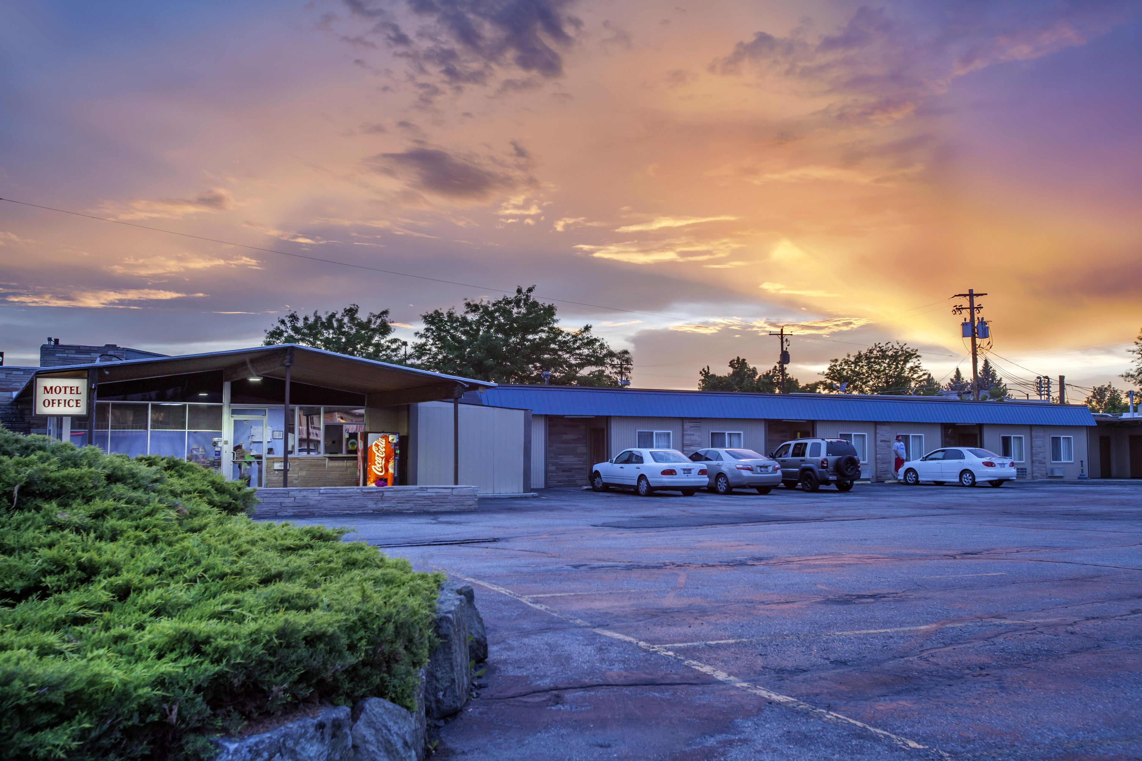 A motel with a parking lot, a Coca-Cola sign, and a clear sky with clouds.