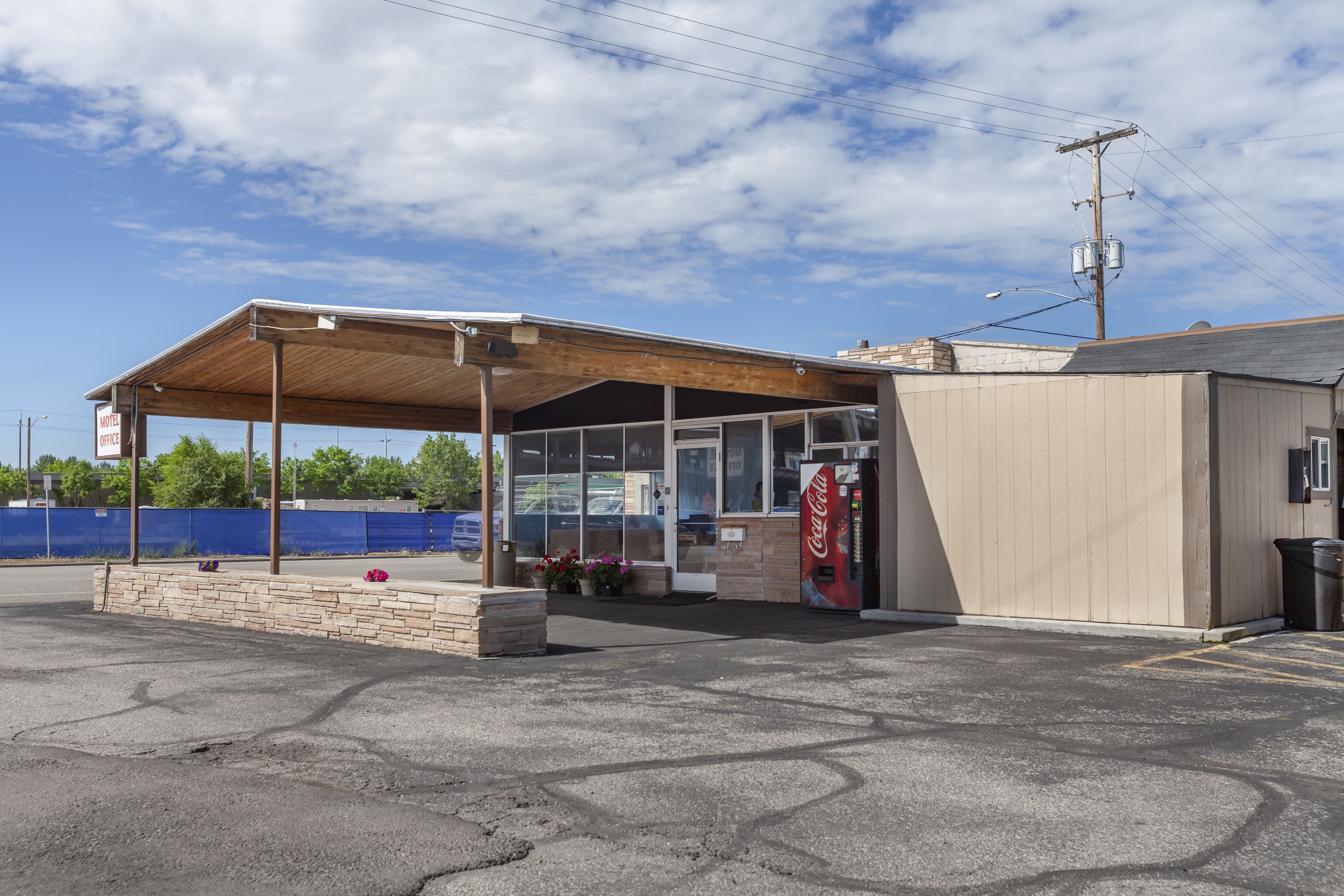 Um motel com área de estacionamento coberta, uma máquina de venda automática de Coca-Cola e um pequeno edifício ao lado do estacionamento.