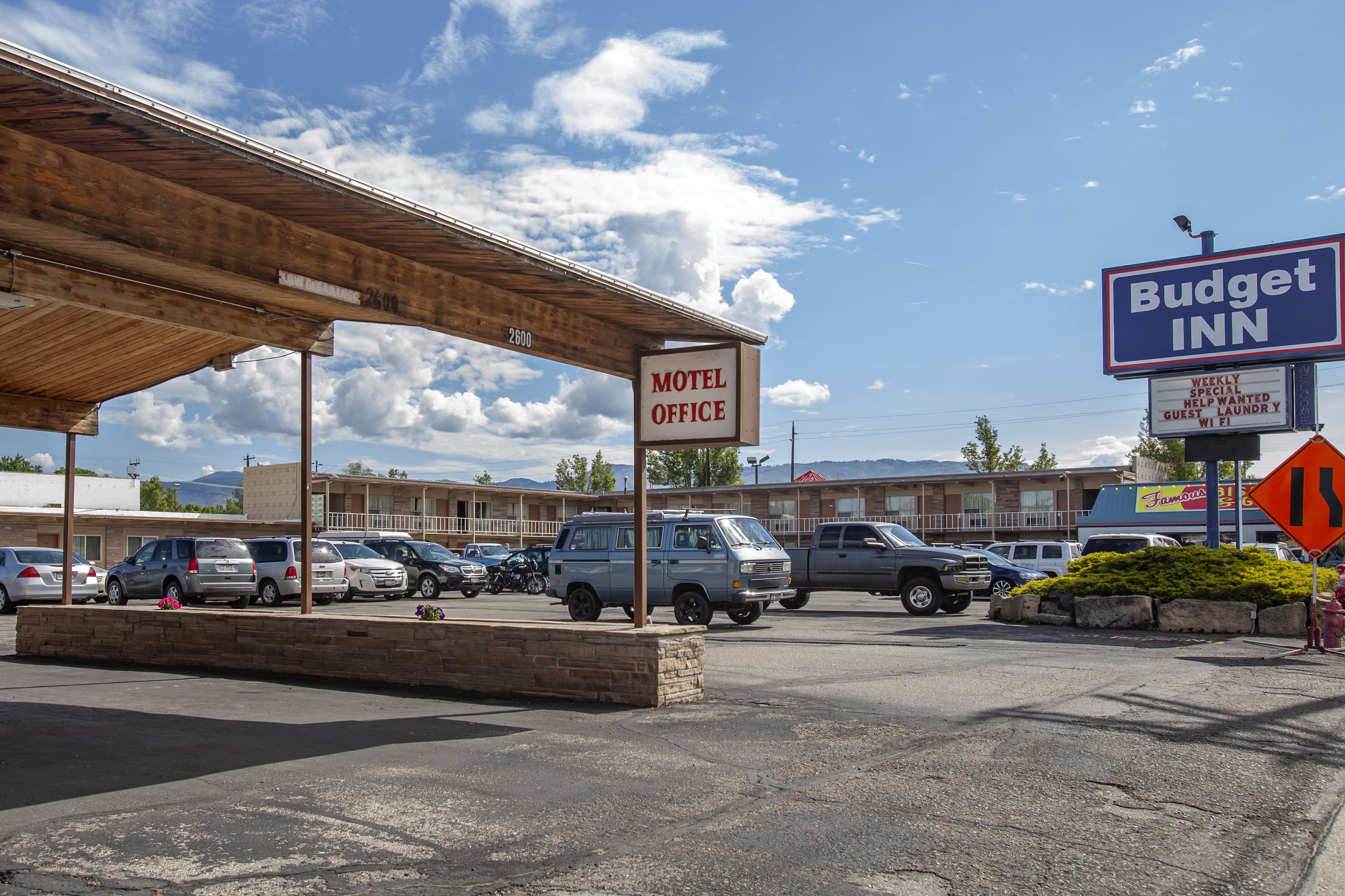 A motel office with a covered parking area, a Budget Inn sign, and a mountain backdrop.
