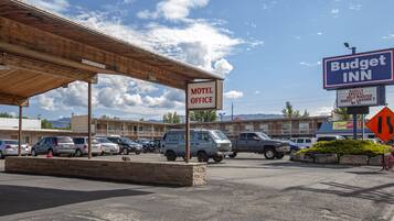 A motel office with a covered parking area, a Budget Inn sign, and a mountain backdrop.