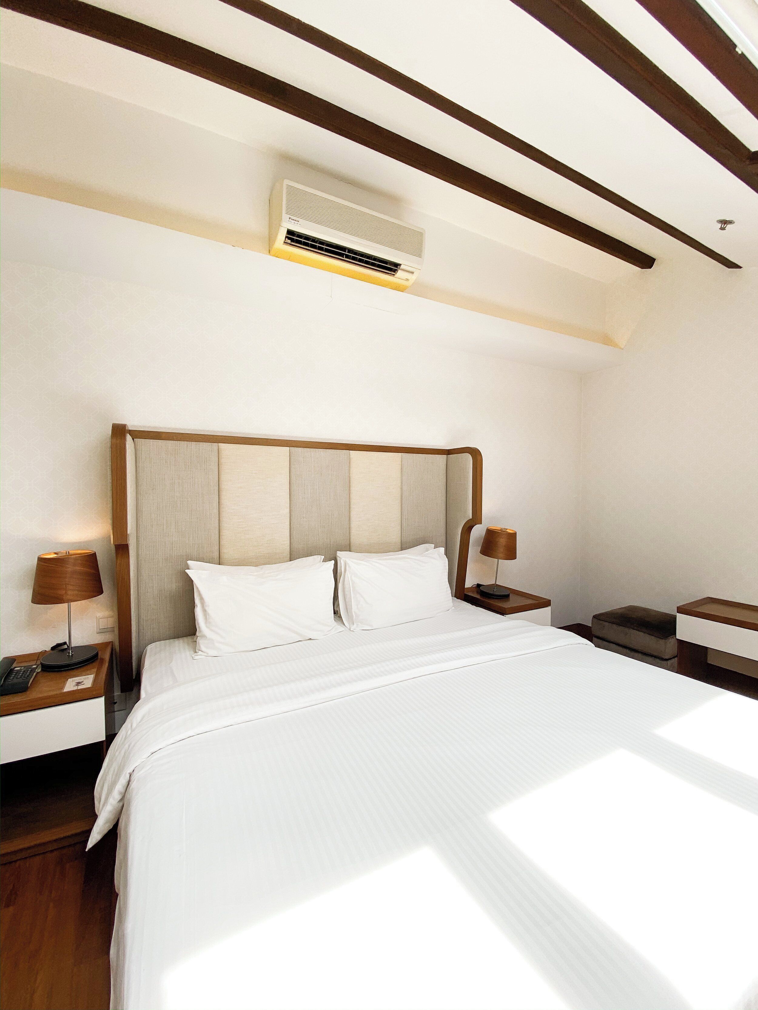 Quarto de hotel com uma cama grande, cabeceira de madeira, mesas de cabeceira com luminárias e um aparelho de ar condicionado no teto.